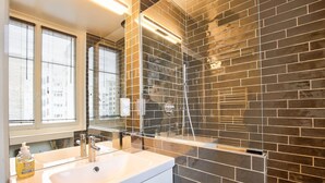 Une salle de bain moderne avec un grand miroir, un lavabo et un espace douche délimité par une paroi en verre.