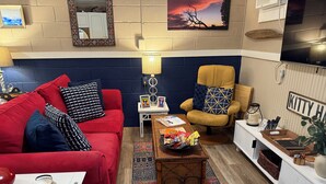 A living room with a red sofa, a yellow armchair, a coffee table with snacks, a TV, and a 'KITTY H' sign. - Awesome suite, 100 steps to the ocean! (Kitty Hawk)