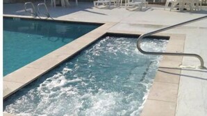 A swimming pool with a water feature, surrounded by lounge chairs and a tiled deck. - Awesome suite, 100 steps to the ocean! (Kitty Hawk)
