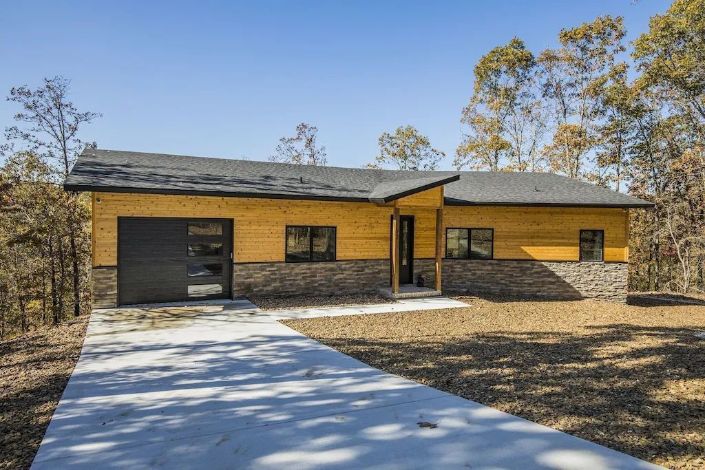 A modern two-story house with a combination of wooden and stone exterior, a driveway, and a clear sky.