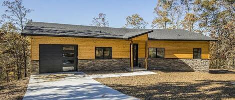 A modern two-story house with a combination of wooden and stone exterior, a driveway, and a clear sky.