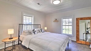 Un dormitorio con una cama, dos mesitas de noche con lámparas, un espejo grande y dos ventanas.