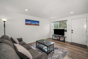 A living room with a sofa, a coffee table with magazines, a TV on a stand, and a painting on the wall.