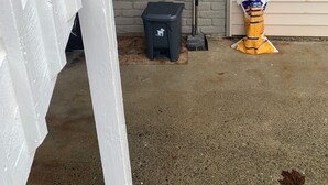Eine Beton-Terrasse mit weißem Zaun, einem schwarzen Müllbehälter, einem Besen und einer Kühlbox mit Eis.