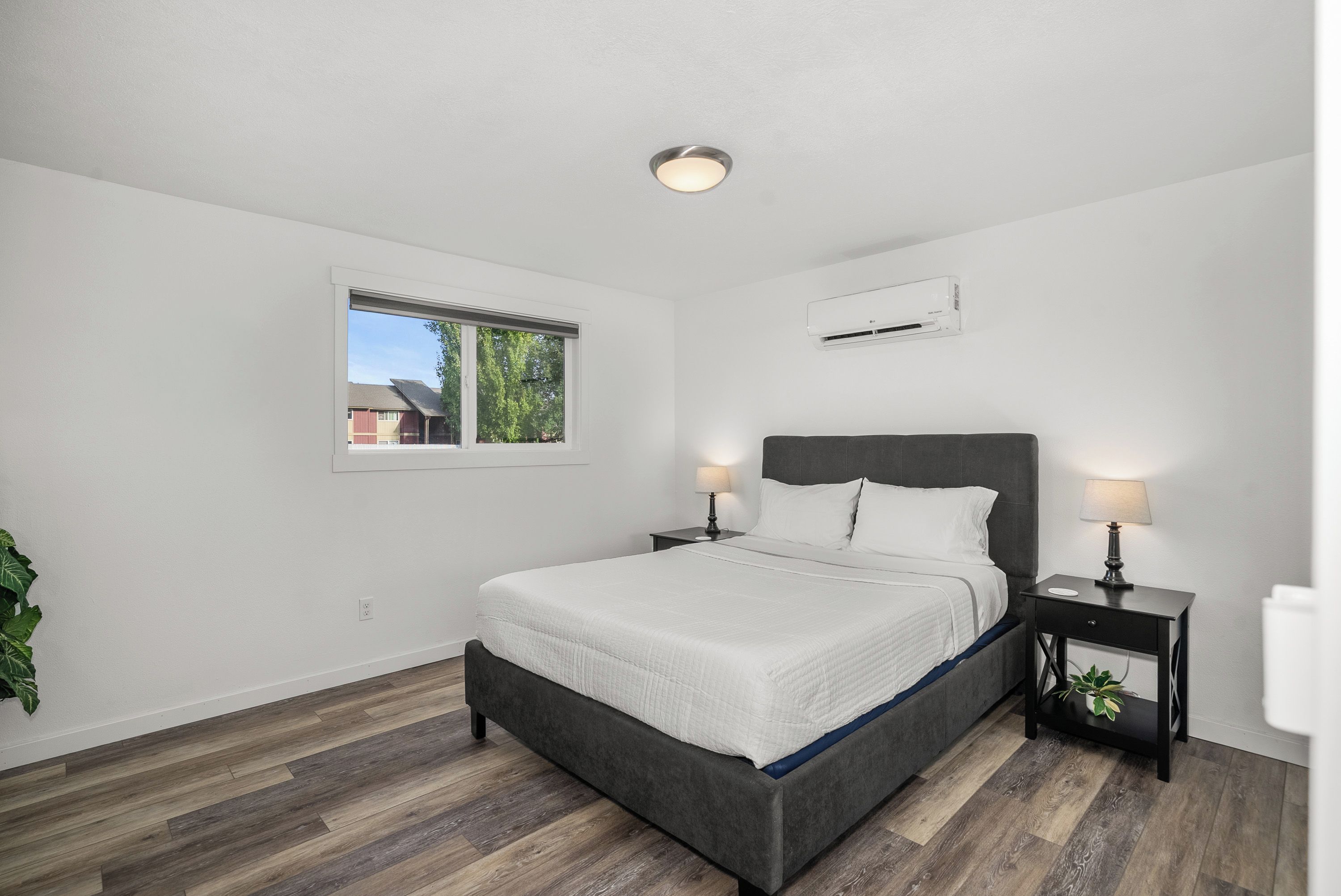 A bedroom with a bed, bedside tables, a window, and an air conditioning unit.