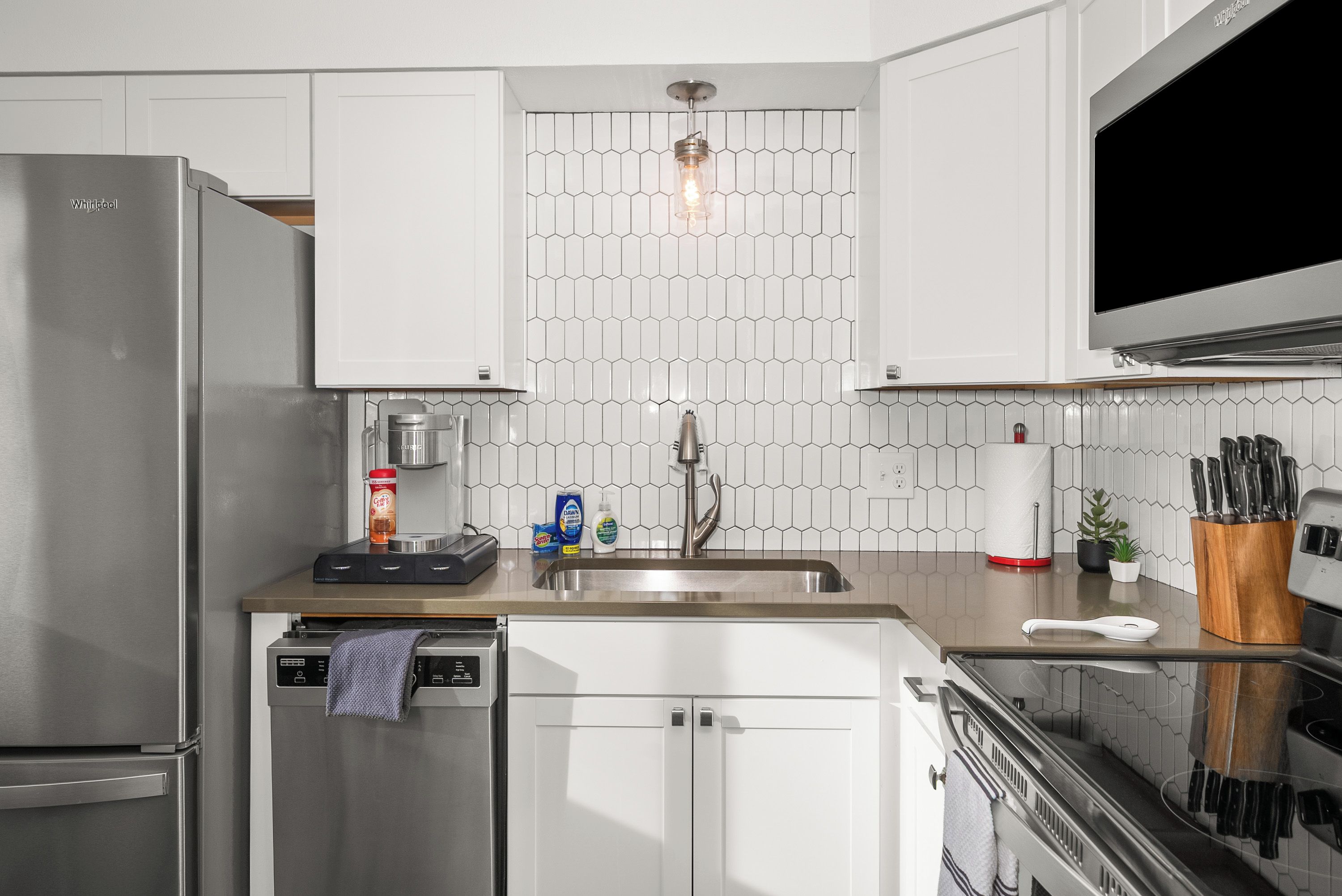 A modern kitchen with white cabinets, a stainless steel refrigerator, a dishwasher, a sink, and a microwave.