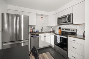 Una cocina moderna con electrodomésticos de acero inoxidable, muebles blancos y salpicadero de azulejos.