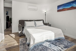 Une chambre à coucher comprenant un lit, une table de chevet, une lampe, un tableau et un couloir menant à une autre pièce.