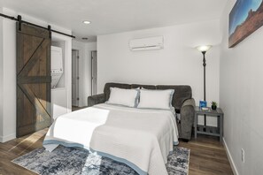 Un dormitorio con cama, mesita de noche, lámpara, puerta corredera y aire acondicionado instalado en la pared.