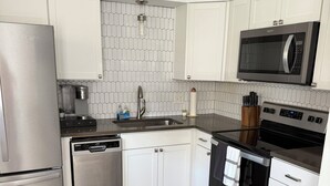 Eine moderne Küche mit weißen Schränken, einem Edelstahl-Kühlschrank, einer Mikrowelle und einem Geschirrspüler.