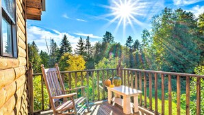 A wooden deck with a rocking chair and a table, overlooking a forested area. - West Danville Cabin: Day Trip to Stowe Mtn! (West Danville)
