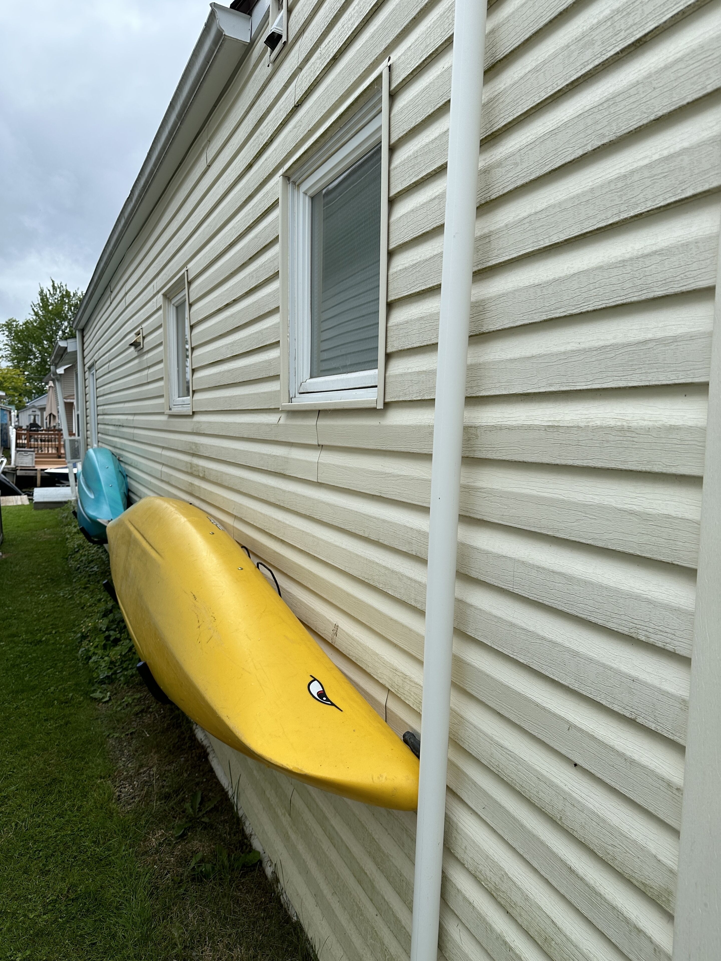 A yellow kayak leaning against a house with white siding and a window.