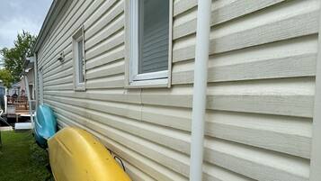 A yellow kayak leaning against a house with white siding and a window.