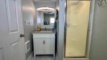 Un baño con tocador blanco, lavamanos y ducha con puerta de cristal.