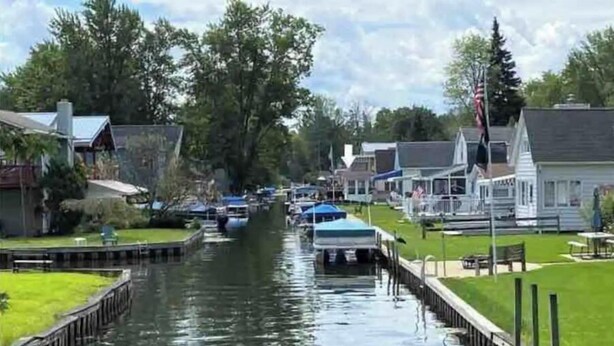 Un canal con barcos, rodeado de casas residenciales y vegetación.