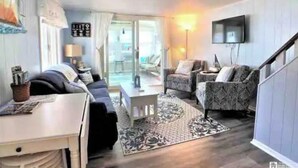 Una sala de estar con sofá, sillón y televisor montado en la pared.