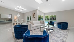 A modern living room with a white sofa, blue armchairs, and a glass coffee table. - BY THE SEA VACATION VILLAS 5 STAR AZUL 3/2 PRIVATE POOL WALK TO BEACH (Fort Lauderdale)
