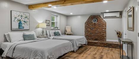 A bedroom with two beds, a brick wall, and a wooden ceiling beam.