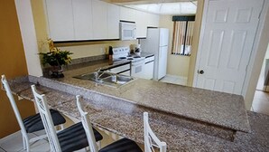 Ett kompakt kök med en bänkskiva i granit, vita skåp och en inbyggd ugn. Det finns fyra barstolar och en krukväxt.