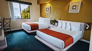 Ett hotellrum med två sängar, ett skrivbord, en stol och ett fönster med utsikt över träd.