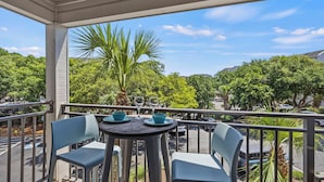 Ein Balkon mit zwei Stühlen, einem Tisch und Blick auf einen Parkplatz und Grünflächen.