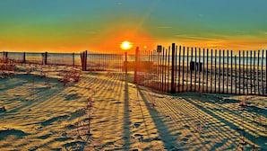 Eine Strandansicht mit Holzzaun, Sandweg und untergehendem Sonnenuntergang im Hintergrund.