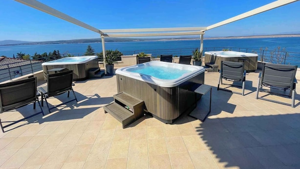 En takterrass med två bubbelpooler, utomhusmöbler och utsikt över havet.
