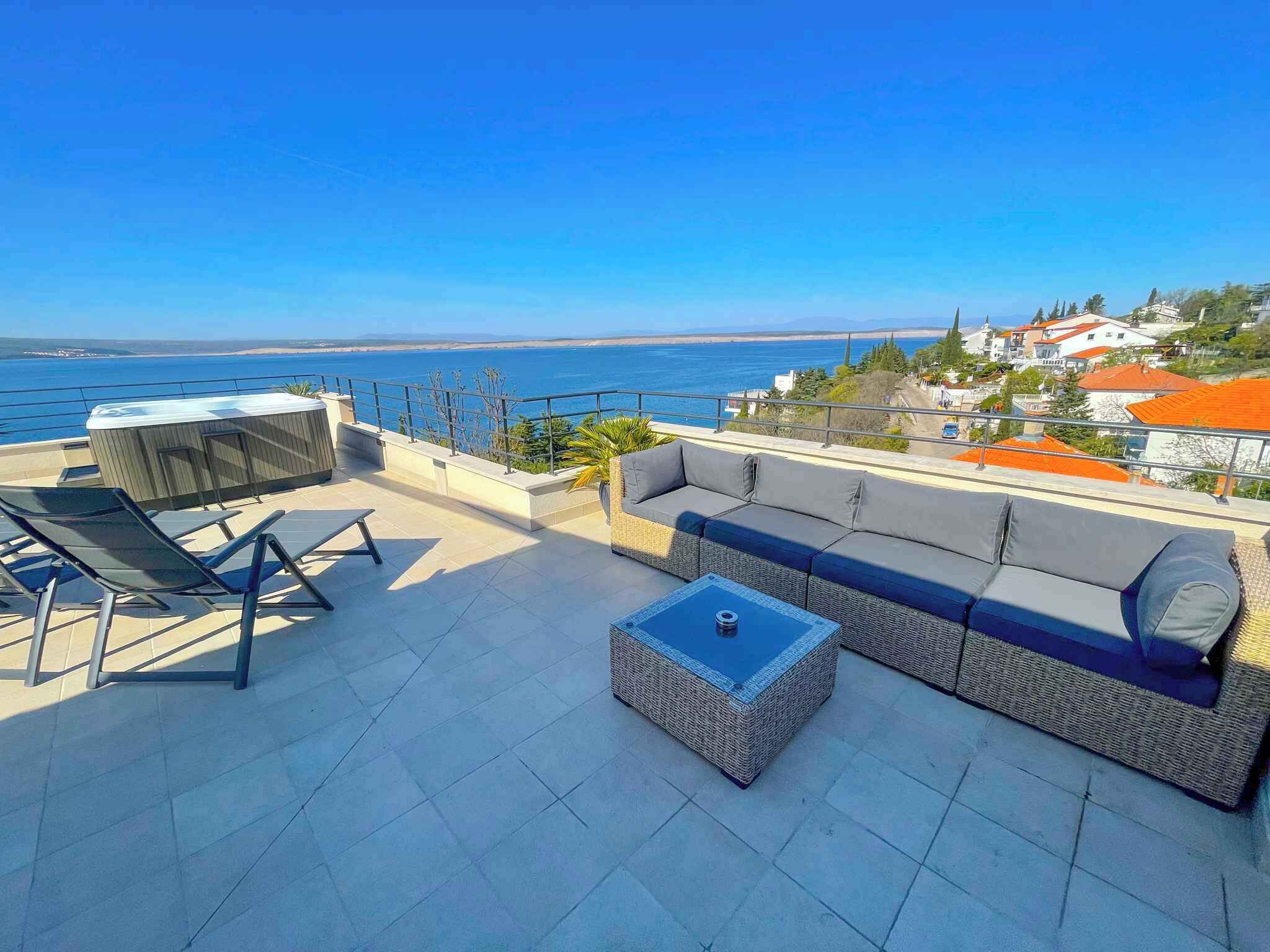 Une terrasse sur le toit, aménagée avec un canapé, des chaises et une table, d’où l’on peut admirer une vue sur la côte.