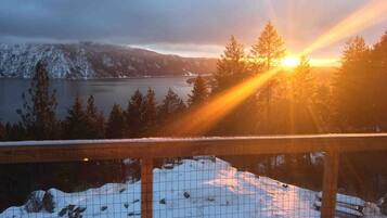 A snowy landscape with a lake, trees, and a wooden fence.