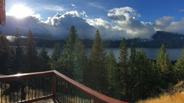 Une vue depuis un balcon donnant sur un lac, avec des arbres et des montagnes en arrière-plan.