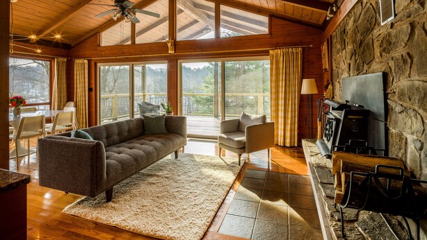 Un salón espacioso con un sofá grande, una mesa de centro y una chimenea. Varias ventanas ofrecen luz natural y vistas al exterior.