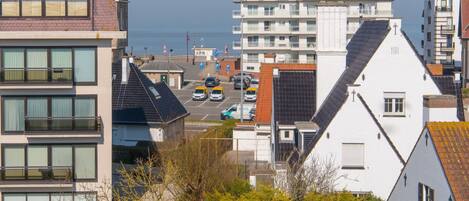 Zona residencial costera con edificios modernos, vista despejada al mar y un aparcamiento con varios coches.