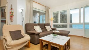 Un salon avec un canapé, un fauteuil et une petite table. Il y a une fenêtre donnant sur la mer.