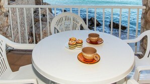 Une table ronde avec deux tasses et deux pâtisseries, posée sur un balcon donnant sur la mer.