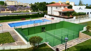 Ein Schwimmbad mit einem grünen Tennisplatz und einem Gebäude mit rotem Dach.