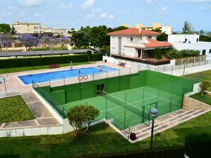 A swimming pool with a green tennis court and a building with a red roof.