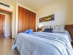 A bedroom with a bed, a wooden wardrobe, a wall art piece, and a nightstand with a lamp.