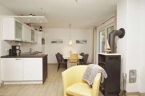 Cocina moderna con armarios blancos, comedor con mesa y sillas, y un ventanal con decoración náutica.