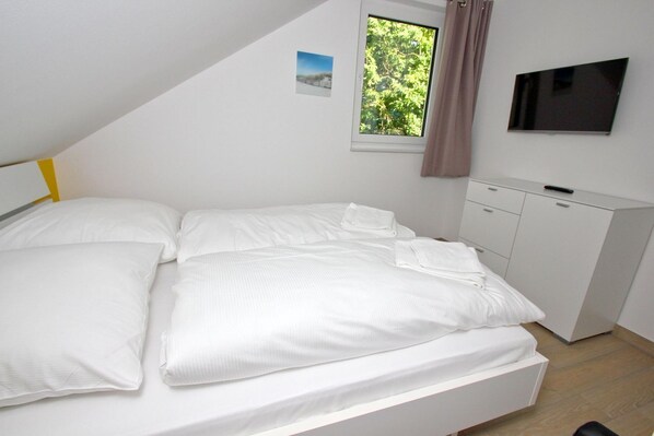 Une chambre à coucher avec un lit, une télévision, une fenêtre donnant sur des arbres et un placard.