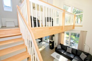 A spacious living area with a wooden staircase, a black sofa, and a dining table.