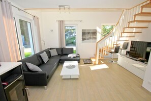 Un salon moderne avec un canapé d’angle noir, une table basse blanche, un téléviseur et un escalier en bois.