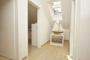 A narrow hallway with a skylight, a small boat model on a shelf, and a wooden floor.