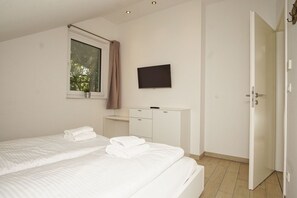 Ein Hotelzimmer mit zwei Betten, einem Fernseher, einem Schreibtisch und einem Kleiderschrank.