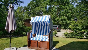 A wooden outdoor chair with a striped canopy, a stone bench, and a patio umbrella.