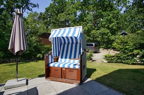 A wooden outdoor chair with a striped canopy, a stone bench, and a patio umbrella.