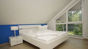 A bedroom with a bed, a nightstand, a lamp, and a large window with a view of greenery.