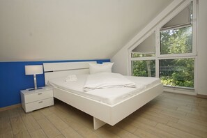 A bedroom with a bed, a nightstand, a lamp, and a large window with a view of greenery.