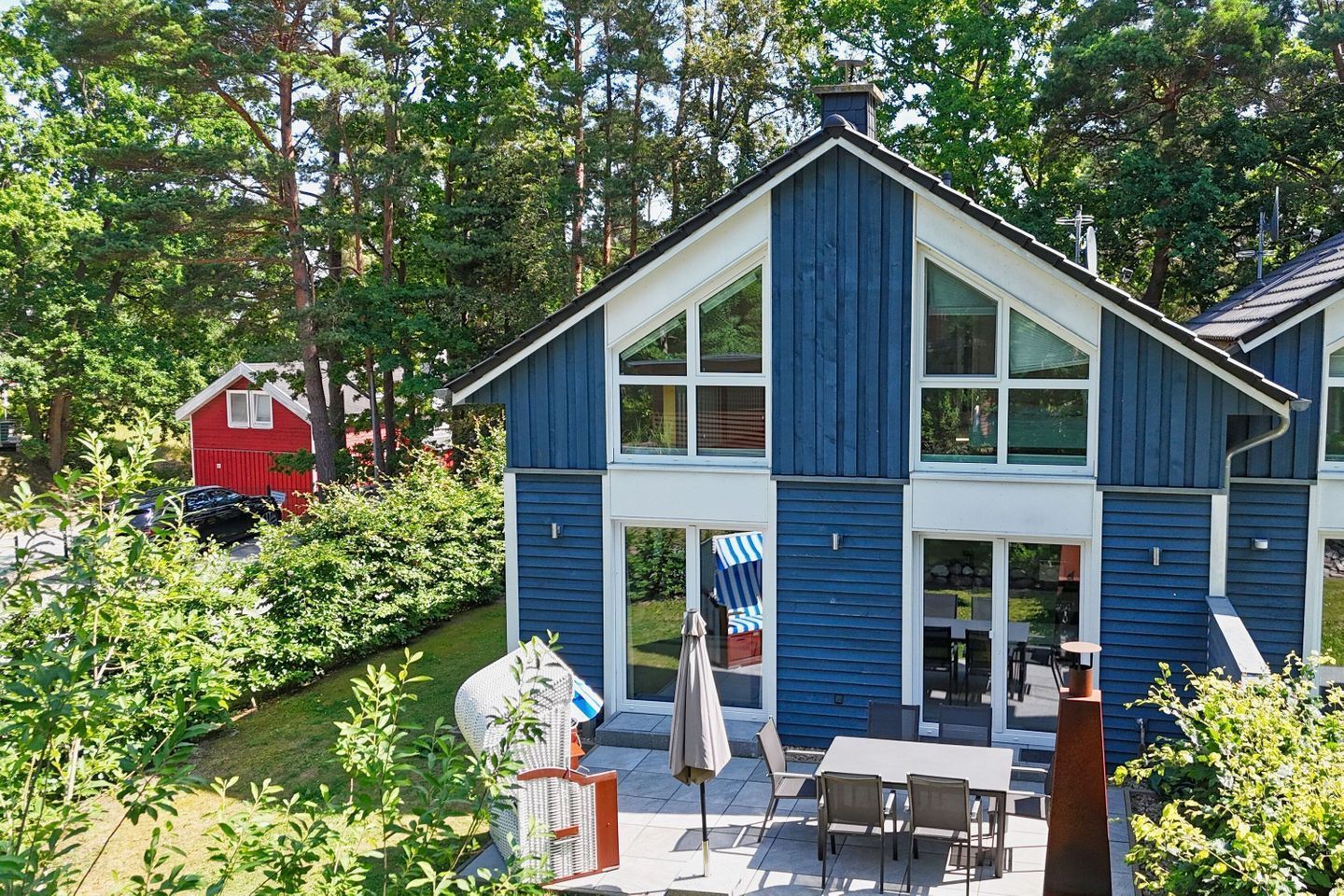 Une maison à deux étages avec une grande véranda à l’avant, un coin repas avec du mobilier d’extérieur, et une grange rouge en arrière-plan.
