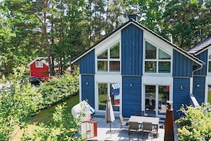 A two-story house with a large front porch, a dining area with outdoor furniture, and a red barn in the background. - House on the Beach Dune - Beachfront Vacation Home with Private Sauna and Fireplace - (Baabe)