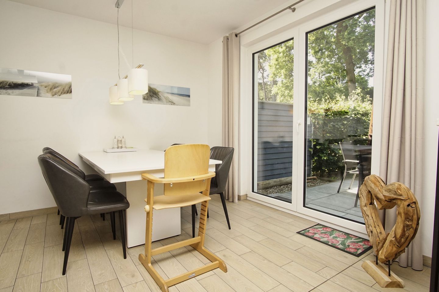 A dining area with a white table, black chairs, a wooden chair, and a view through a glass door to the outside.
